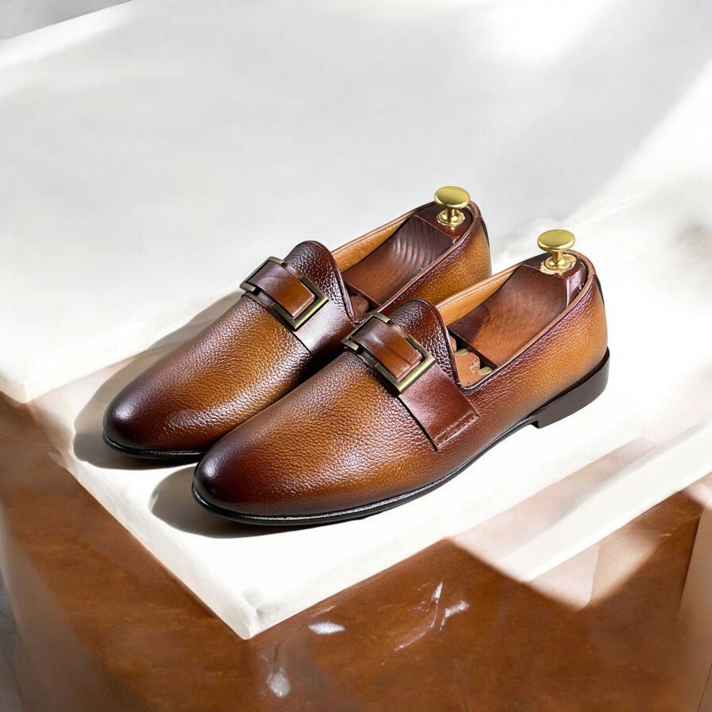 These elegant brown leather loafers are crafted from high-quality full-grain leather with a rich, dual-tone gradient finish. Featuring a sleek slip-on design, they offer both sophistication and comfort. The shoes are adorned with a stylish metal-buckled strap, adding a refined touch to their classic silhouette. 

The interior is lined with premium leather for breathability and durability, while the cushioned insole ensures all-day comfort. The sturdy black outsole provides excellent grip and longevity. Idea